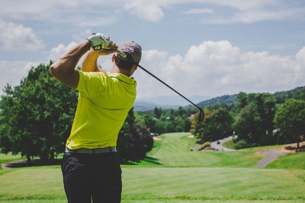 A golfer mid-swing on a tree-lined course